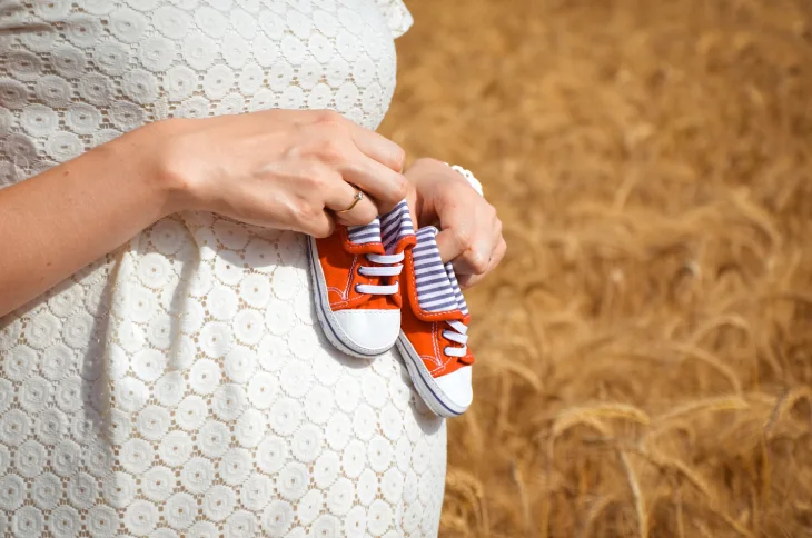 Baby Shoes Business Names Ideas - a pregnant woman holding orange baby shoes on her stomach